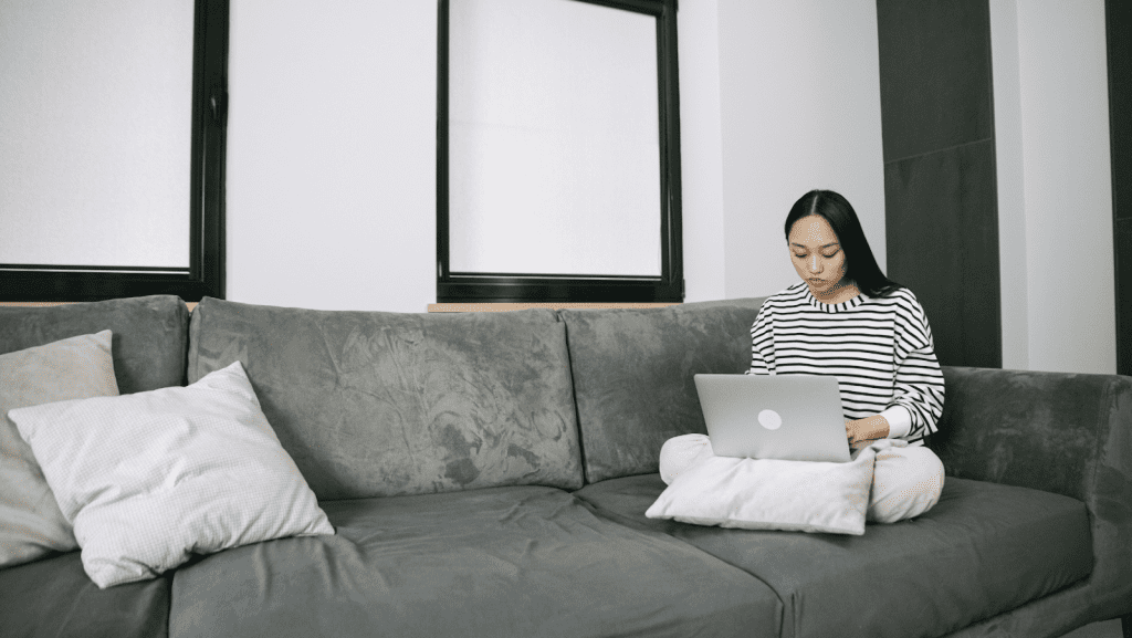 Woman sitting on a gray couch with a laptop